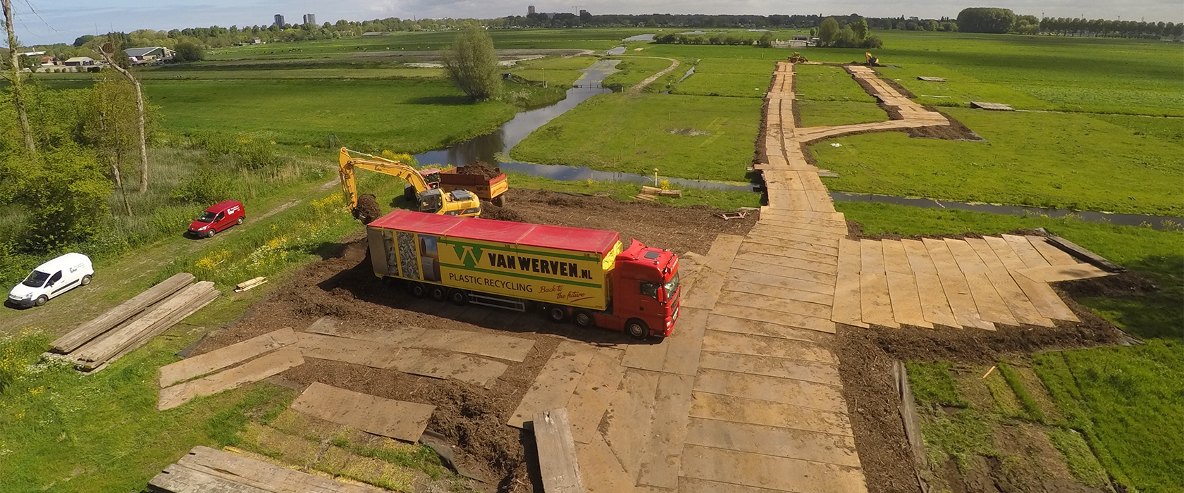 Luchtfoto van de houten rijbaan door het weiland, met vrachtwagen en rupskraan