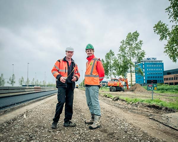 Twee medewerkers in oranje werkkleding en helm op het werk aan de verbrede op- en afrit van de A6 bij Lelystad