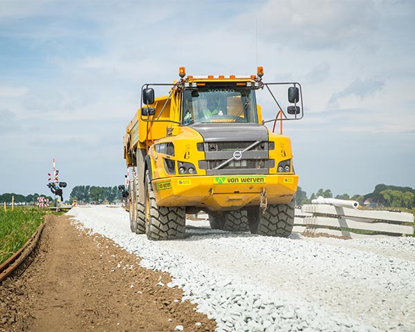 Knikdumper van Van Werven rijdt over een pas aangelegde steenslagbaan langs een spoorwegovergang