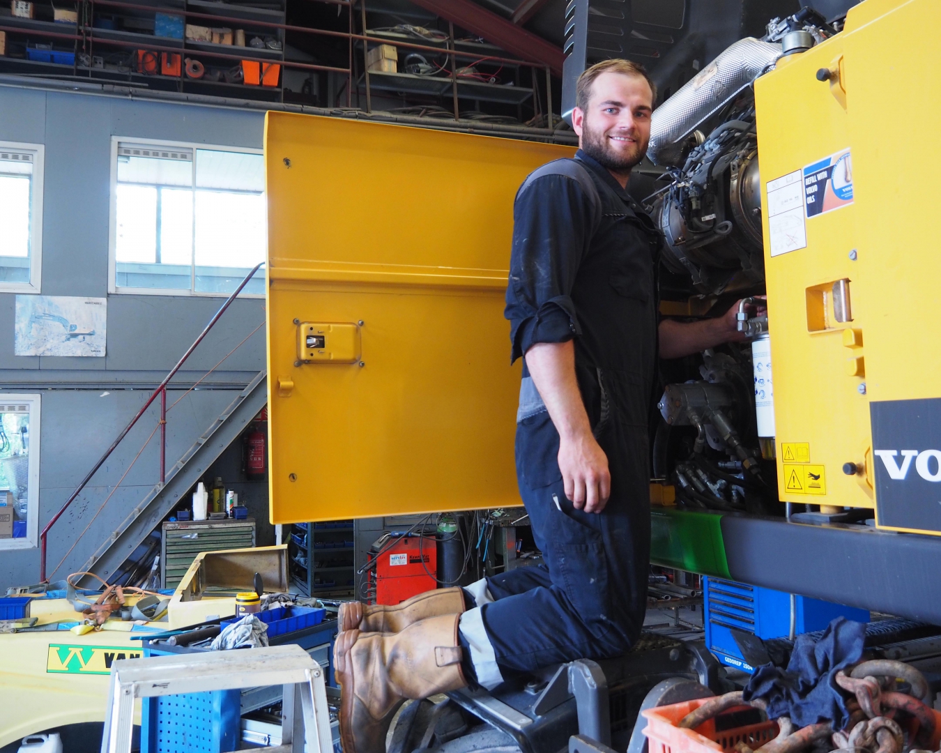 Monteur werkt aan de opengeklapte motorkap van een graafmachine in de werkplaats