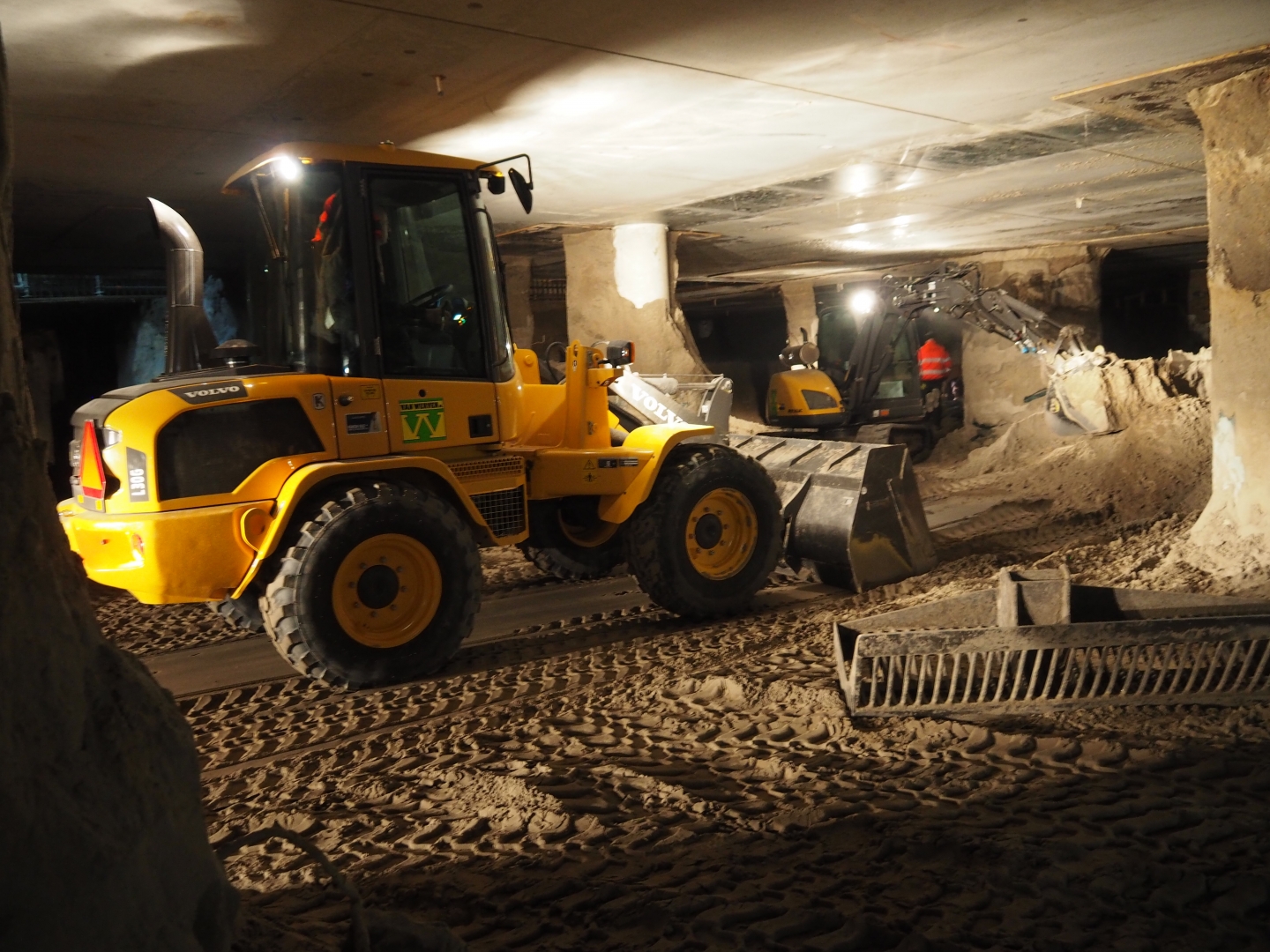 Wiellaadschop en graafmachine werken onder een bestaand gebouw in een verlichte ondergrondse ruimte