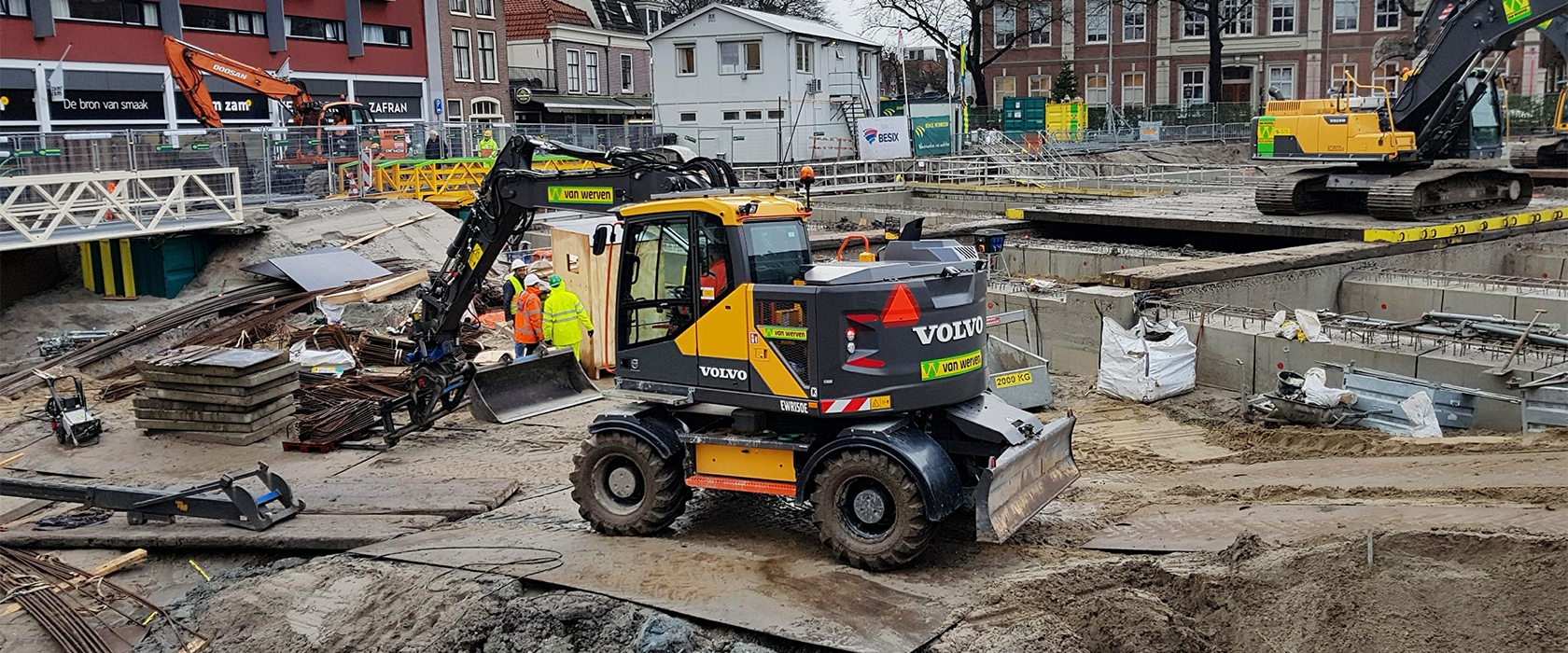 Mobiele graafmachine van Van Werven werkt in een bouwkuip midden in een woonstraat